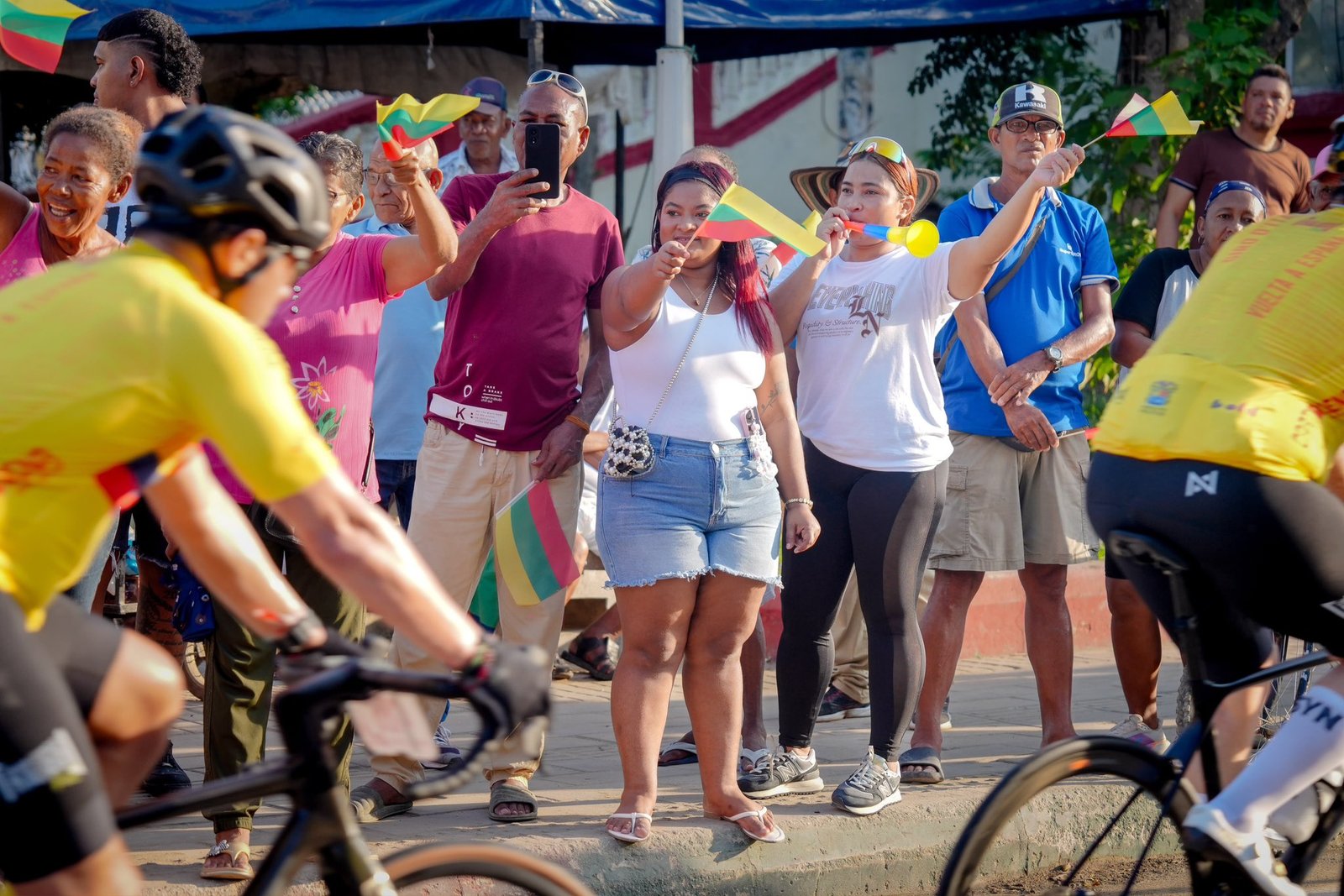 Mujeres con banderas de Bolívar animan a los ciclistas desde la orilla de la carretera