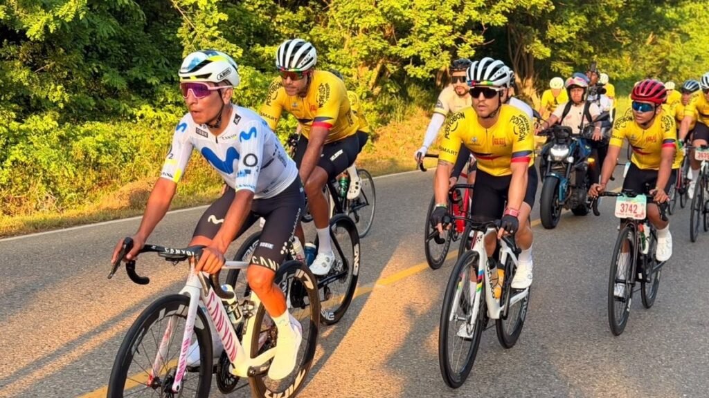 Nairo Quintana, con uniforme blanco, rueda junto a ciclistas con camisetas amarillas por una carretera rodeada de árboles en Bolívar