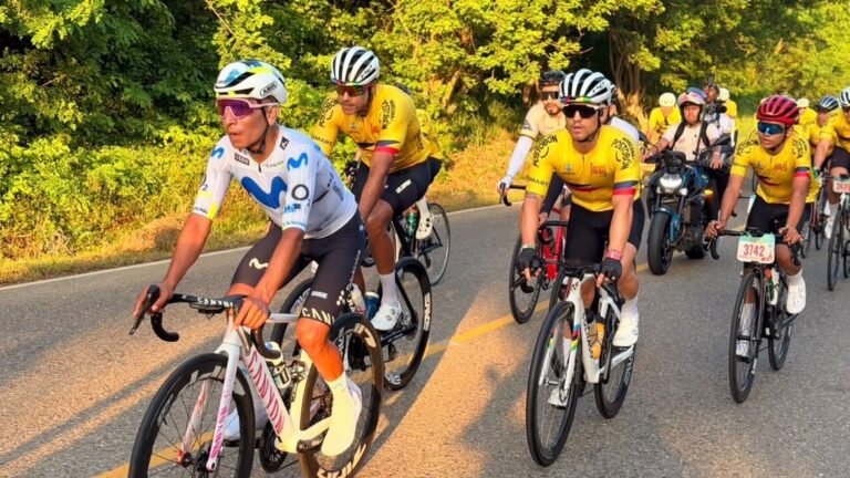 Nairo Quintana, con uniforme blanco, rueda junto a ciclistas con camisetas amarillas por una carretera rodeada de árboles en Bolívar