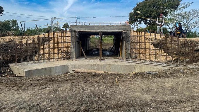 Box culvert de concreto en construcción en la vía de El Zapatero, con varillas de hierro a los lados y un habitante observando desde arriba