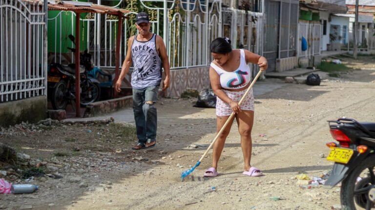 Una mujer barre frente a su casa en una calle destapada de El Pozón mientras un vecino camina a su lado