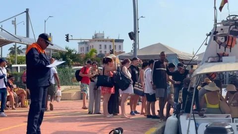 Funcionario de la Dimar revisa documentos en un muelle de Cartagena mientras turistas hacen fila para abordar una lancha