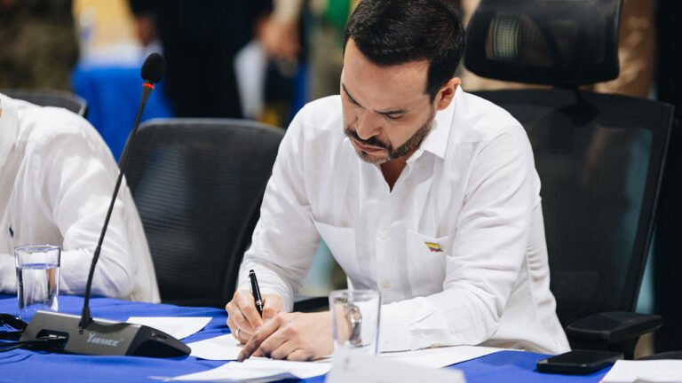 El presidente Abelardo De La Espriella firma un documento sentado en una mesa de trabajo con micrófono