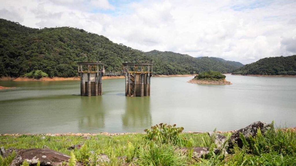Torres de captación de un embalse rodeado de montañas verdes, con el nivel del agua visible en las orillas