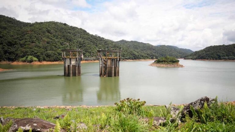 Torres de captación de un embalse rodeado de montañas verdes, con el nivel del agua visible en las orillas