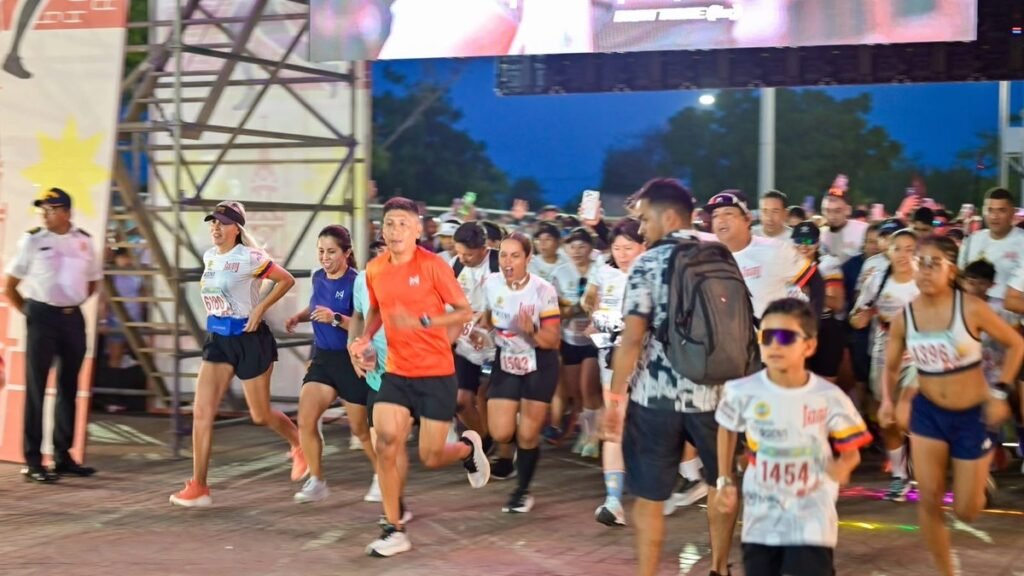 Decenas de corredores, entre ellos un niño con gafas, toman la salida de una carrera en Cartagena ante un escenario con pantalla