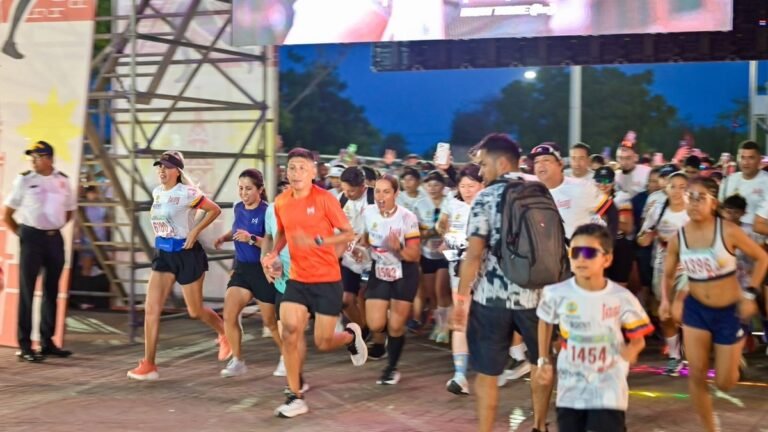 Decenas de corredores, entre ellos un niño con gafas, toman la salida de una carrera en Cartagena ante un escenario con pantalla