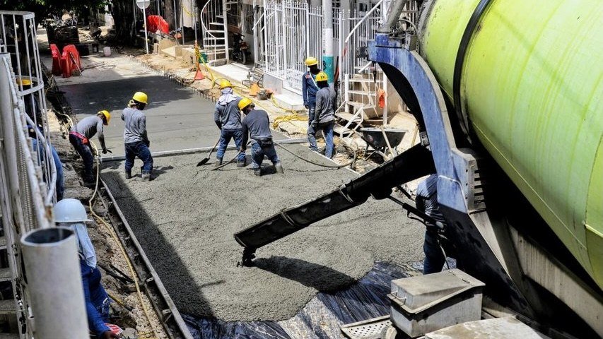 Trabajadores funden pavimento rígido con una mezcladora de concreto en la vía alterna de la Carrera 90A, en Villa Estrella