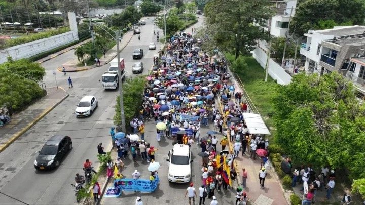 Vista aérea de una marcha con cientos de personas, sombrillas y pancartas avanzando por una avenida arborizada de Cartagena