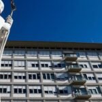 Fachada del Policlínico Gemelli de Roma bajo un cielo azul, con la estatua blanca de un papa en primer plano